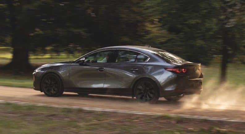 A gray 2021 Mazda3 is shown from the side driving on a dirt road.