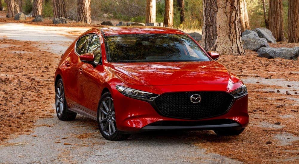 A red 2021 Mazda3 is parked on a road in the woods.