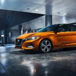 An orange 2021 Nissan Sentra is parked in front of a modern building at night.