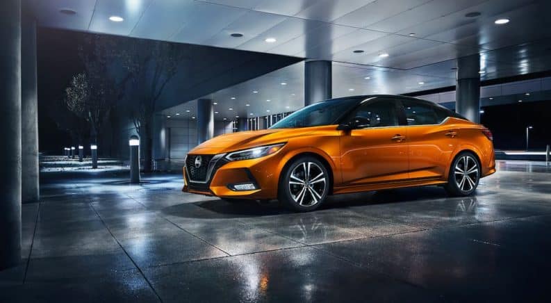 An orange 2021 Nissan Sentra is parked in front of a modern building at night.