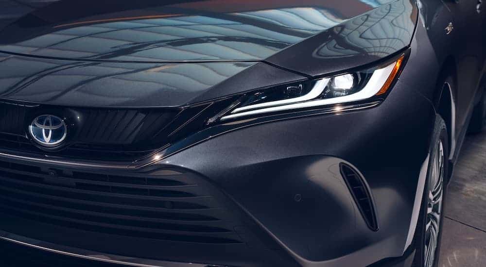 A close up shows the illuminated DRLs and headlight on a dark grey 2021 Toyota Venza.