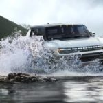 A white 2022 GMC Hummer EV Truck is driving through water.