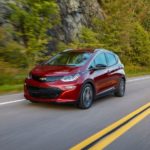 A maroon 2017 Chevy Bolt EV is driving past a large rock face.