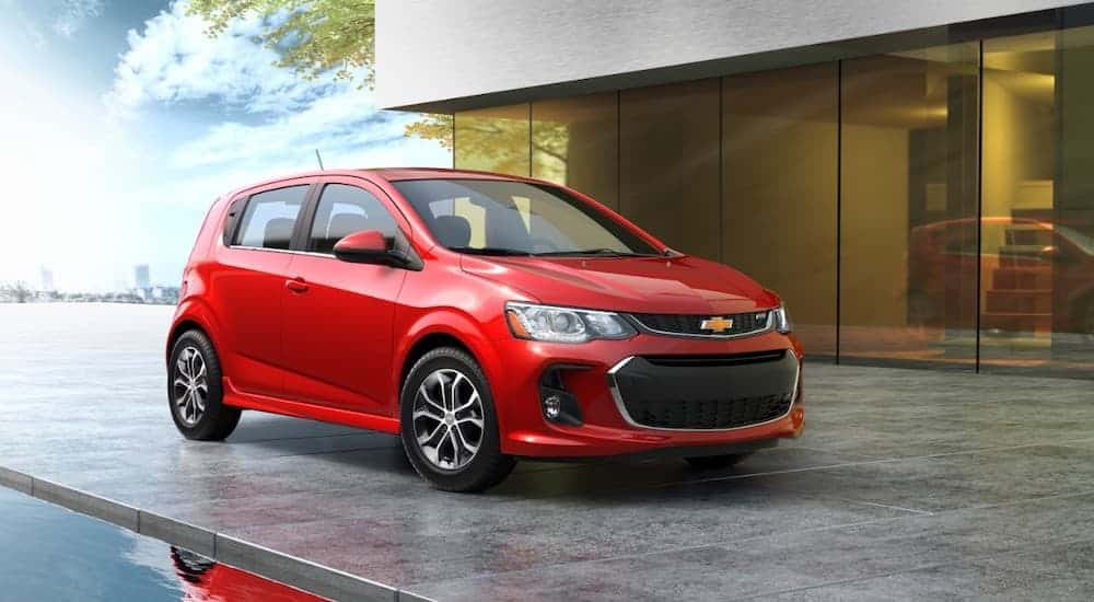 A red 2018 Chevy Sonic is shown from the side parked in front of a modern home.