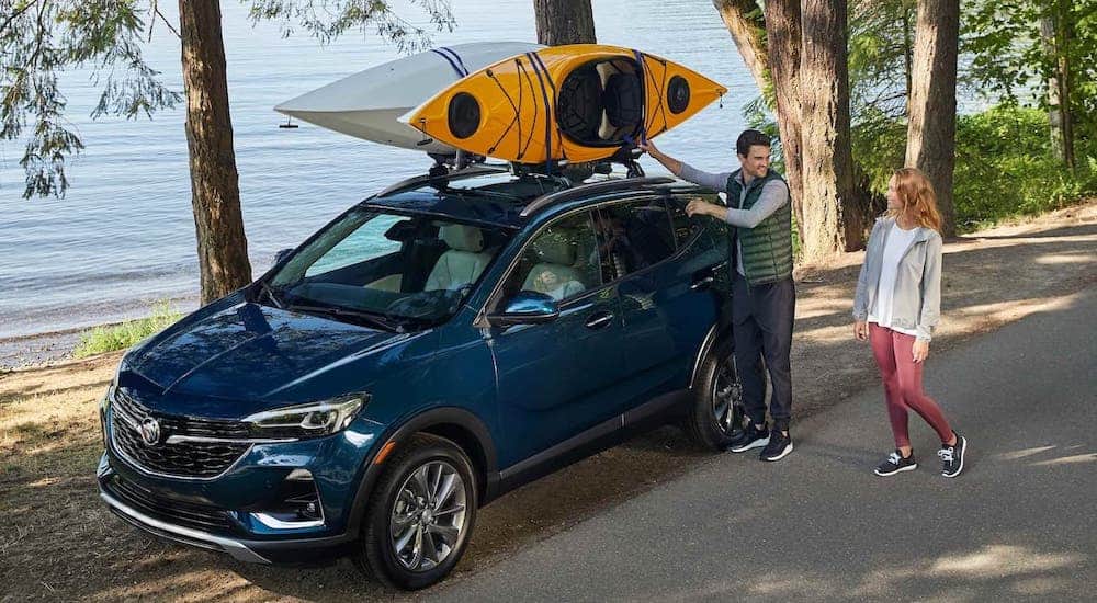 A couple is unloading kayaks off of a blue 2021 Buick Encore GX that is parked in front of a lake.