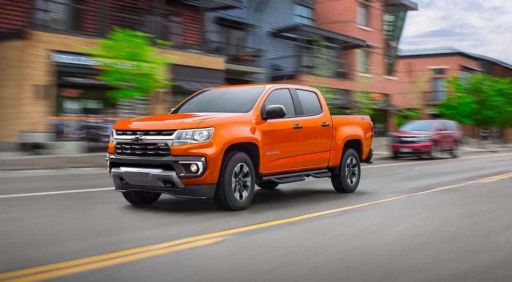 An orange 2021 Chevy Colorado is driving on a city street after leaving a local Chevy car dealer.