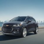 A black 2021 Chevy Trax is driving on a highway away from a city.
