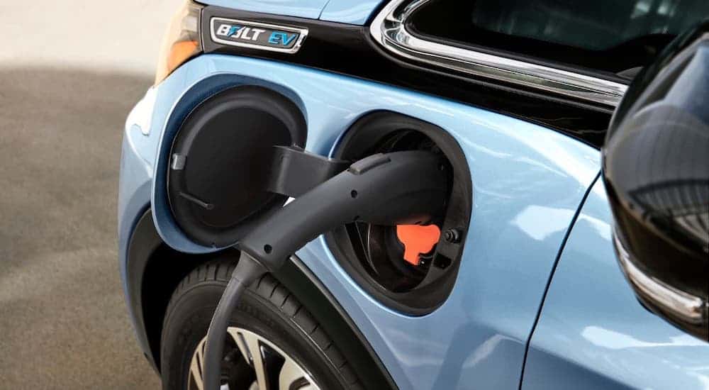 A closeup shows a charger plugged into a Chevy EV, a light blue 2021 Chevy Bolt EV.