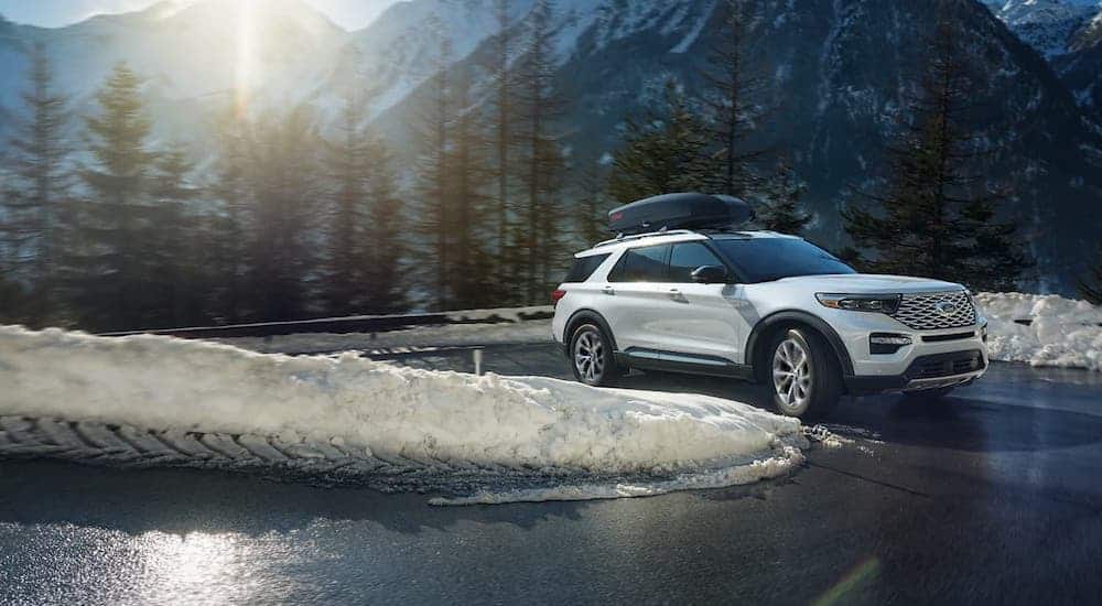 A white 2021 Ford Explorer Platinum is driving on a winding snowy road after leaving a Ford Explorer dealer.