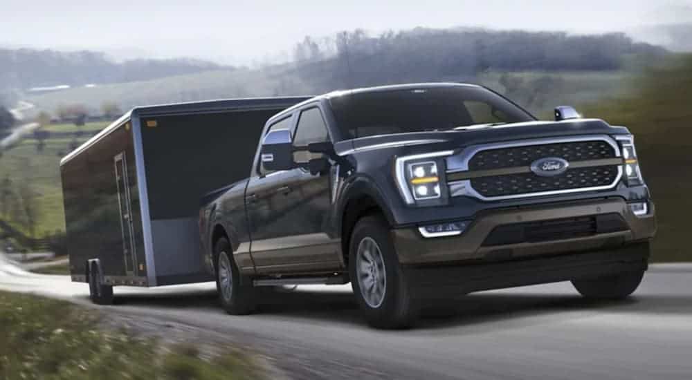 A black 2021 Ford F-150 is towing a black enclosed trailer uphill.