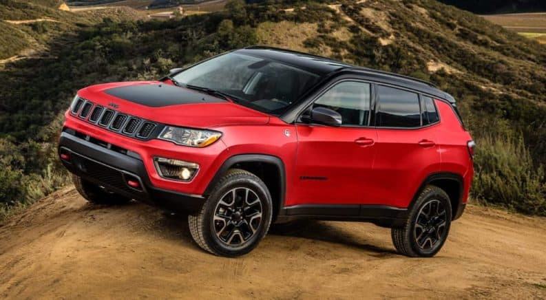 A red 2021 Jeep Compass Trailhawk is parked at the top of a dirt trail on a hill.