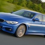 A blue 2017 BMW 4 Series is driving on a rural highway after leaving a used car dealer.
