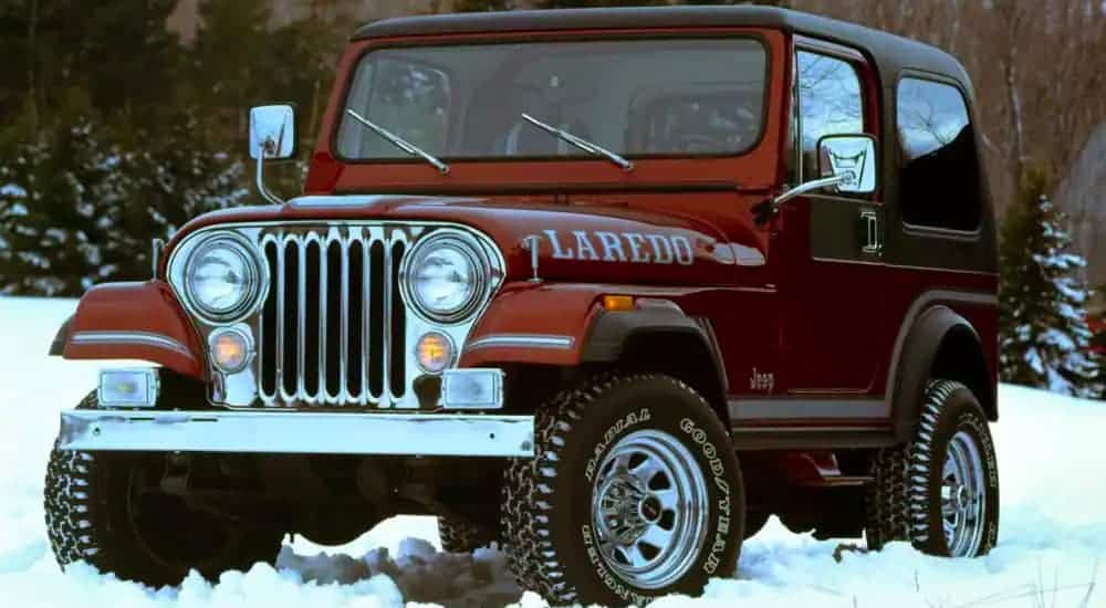 A dark red 1980s Jeep Wrangler Laredo is parked on snow.