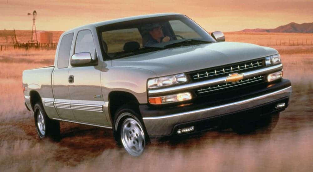 A popular used Chevy truck, a silver 2000 Chevy Silverado 1500, is driving in a grassy field.