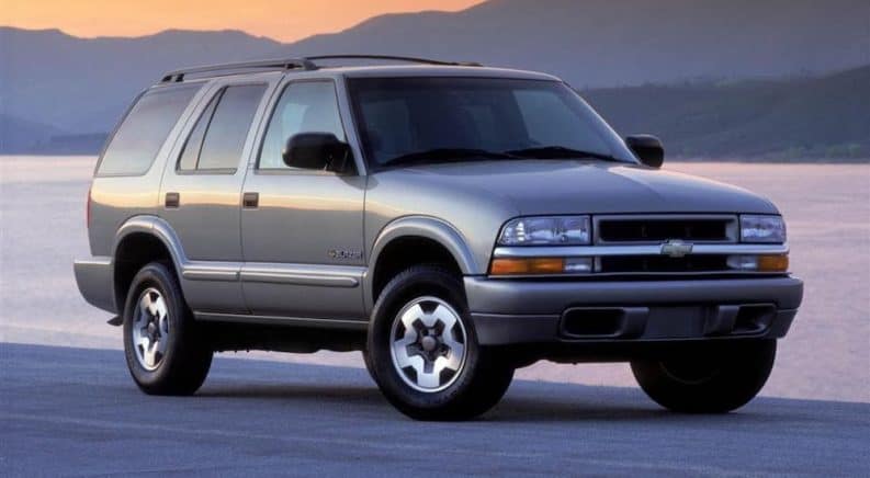A silver 2004 Chevy Blazer is parked in front of a lake and distant mountains.