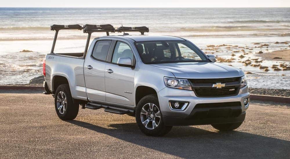 A silver 2016 Chevy Colorado crew cab with a truck rack is parked in front of a beach.