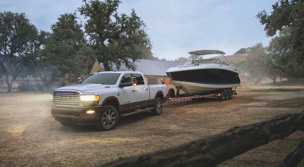 A white 2020 Ram 2500 with a boat on a trailer is parked in front of a cabin.
