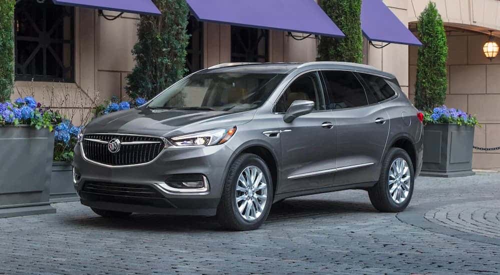 A silver 2021 Buick Enclave is parked in front of a store on paver pathway.