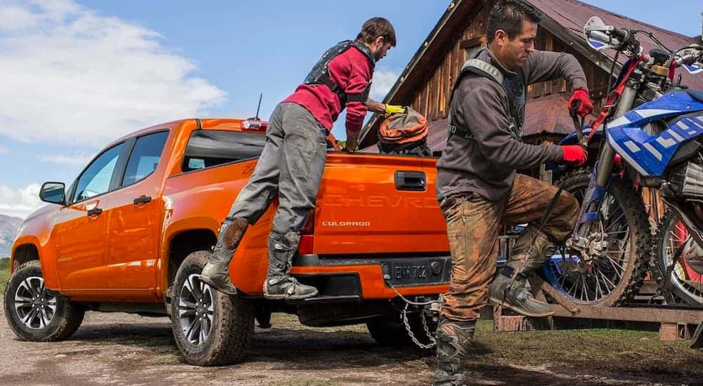 A close up shows two people loading dirt-bikes on the trailer attached to an orange 2021 Chevy Colorado.