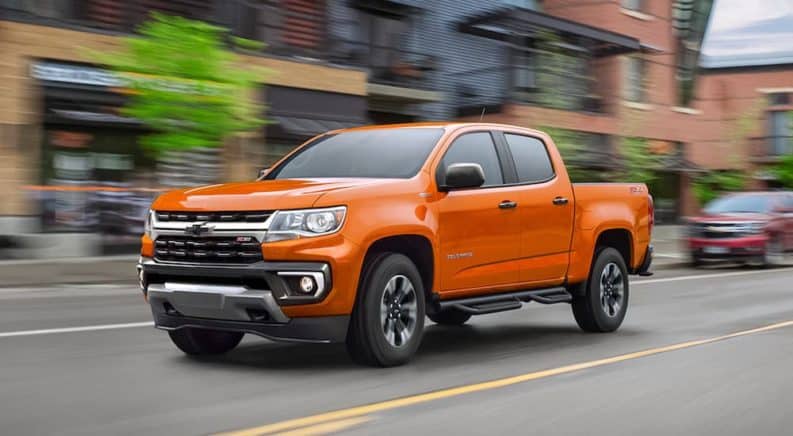 An orange 2021 Chevy Colorado is shown from the side driving past blurred buildings.