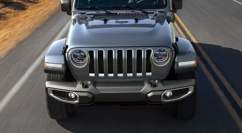 A close up shows silver 2021 Jeep Wrangler 4xe from the front driving down the highway,