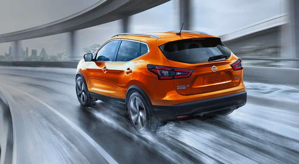 An orange 2021 Nissan Rogue Sport is shown from the rear driving on a wet bridge.
