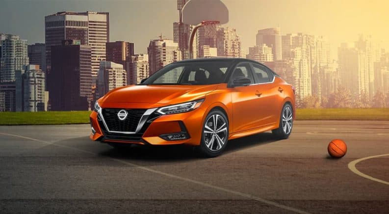 An orange 2021 Nissan Sentra is shown parked on a basketball court with a city skyline in the background.