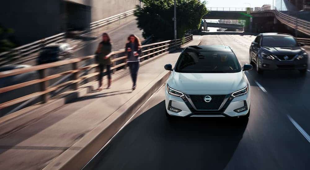 A white 2021 Nissan Sentra is shown driving next to a sidewalk with people walking.