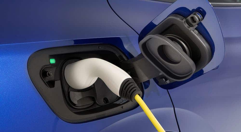 A closeup shows a white charger in the charging port of a dark blue 2021 Volkswagen ID.4.
