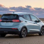 A light blue 2022 Chevy Bolt EV is shown from the rear on a beach at sunset after leaving an Electric Car Dealer.