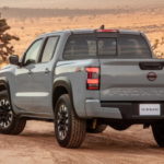 A grey 2022 Nissan Frontier shown from the back is driving through the desert.