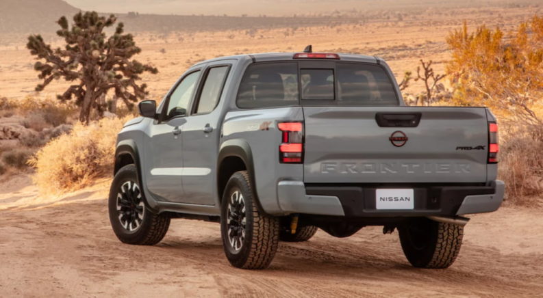 A grey 2022 Nissan Frontier shown from the back is driving through the desert.