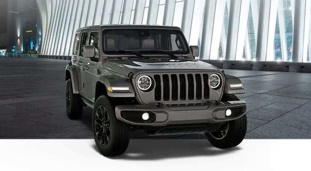 A gray 2021 Jeep Wrangler Unlimited High Altitude is parked in front of a modern building at night.