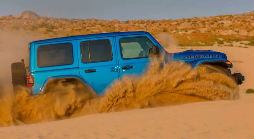 A blue 2021 Jeep Wrangler Unlimited Rubicon 392 is shown from the side kicking up sand after leaving a Black Forest Jeep dealer.