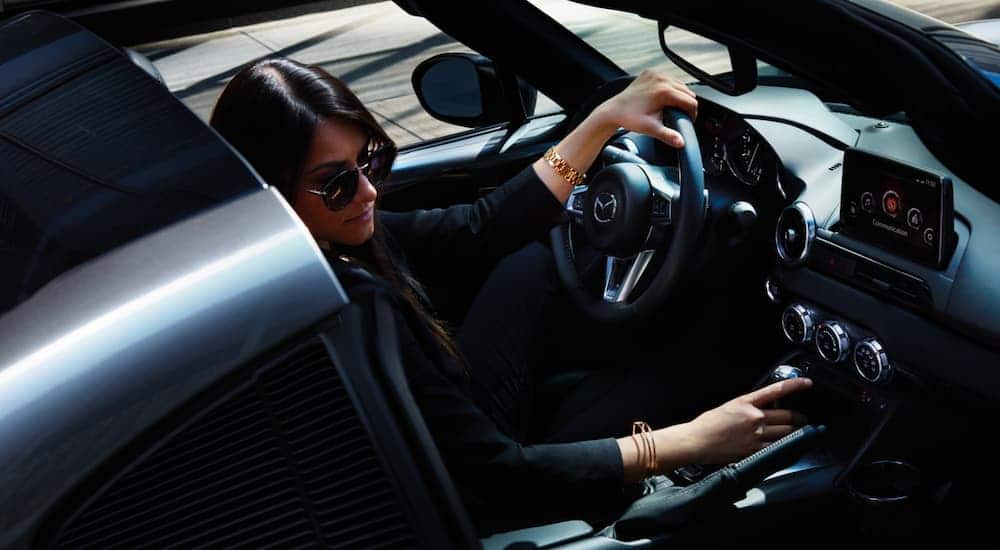 A woman is sunglasses is shown from a high angled sitting in a 2021 Mazda MX-5 Miata RF.