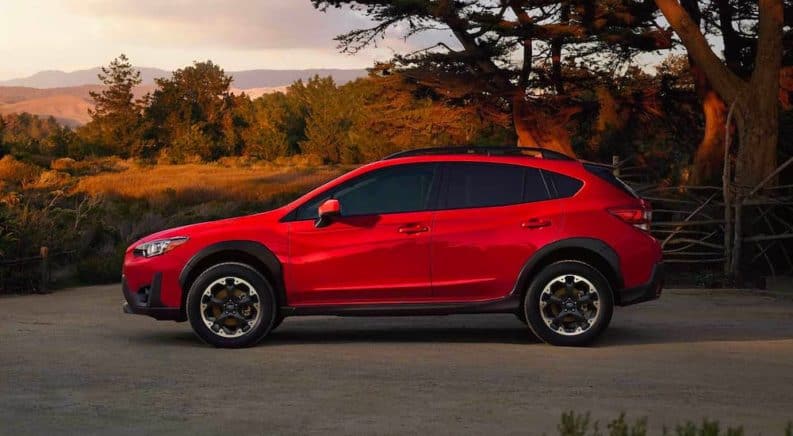 A red 2021 Subaru Crosstrek Hybrid is shown from the side, parked in a gravel lot, after leaving a Subaru dealer.