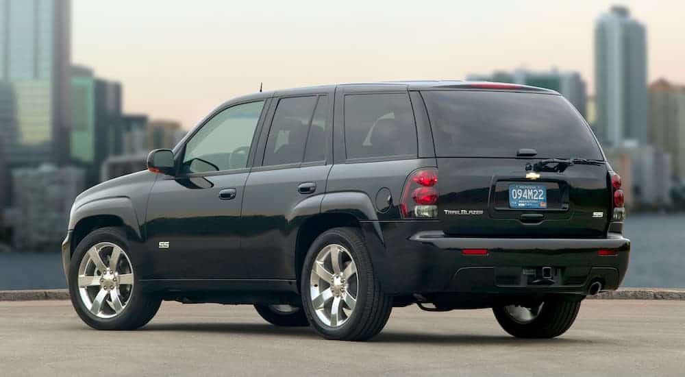 A black 2006 Chevy Trailblazer SS is shown from the rear with a blurred city skyline in the background past a lake.
