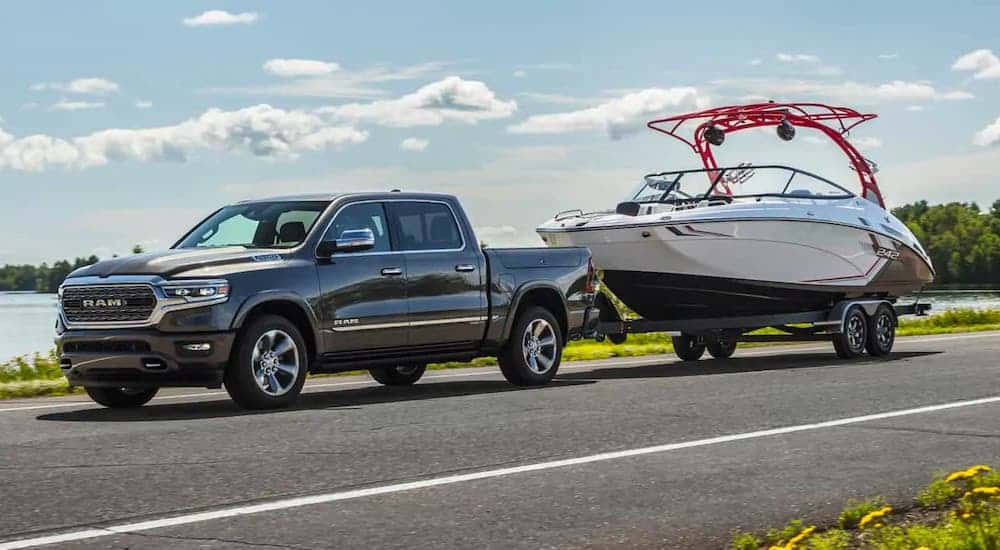 A dark gray 2021 Ram 1500 is towing a boat in front of a lake.