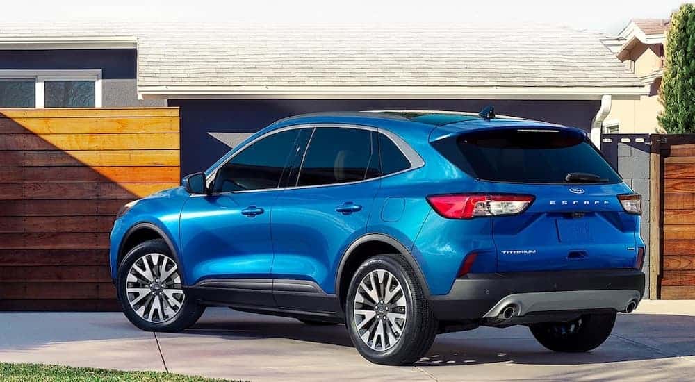 A blue 2021 Ford Escape Titanium is parked in the driveway of a modern house.