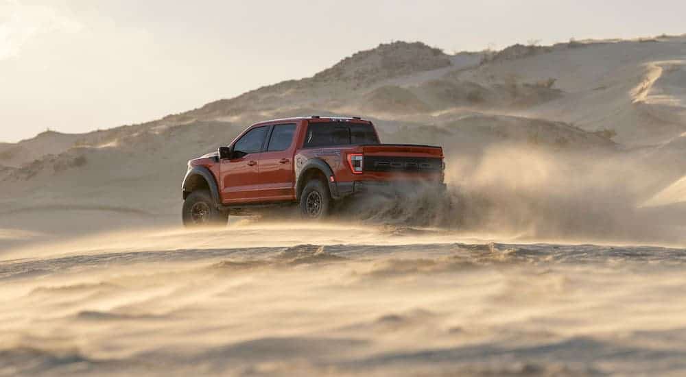 A red and black 2021 Ford F-150 Raptor is shown from the rear kicking up dust in the desert.