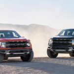 A red and black 2021 Ford F-150 Raptor are parked on the dirt with the front ends angled toward each other.