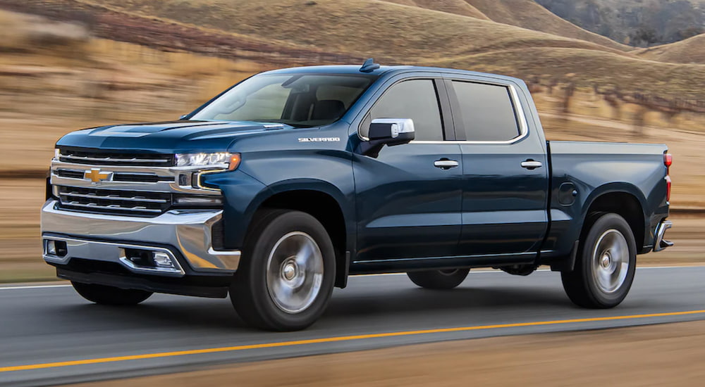 A blue 2021 Chevy Silverado 1500 is shown from the side driving past a vineyard.