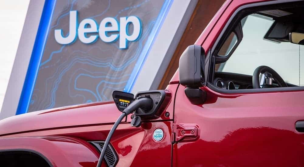 A closeup shows a charger plugged into a red 2021 Jeep Wrangler 4xe.