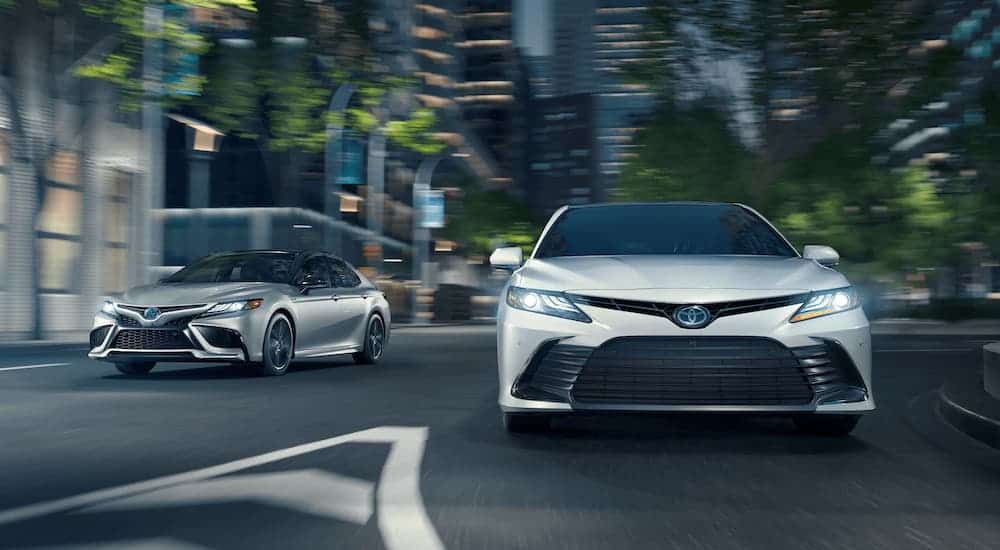 A white and a silver 2021 Toyota Camry are driving on a city street at night.