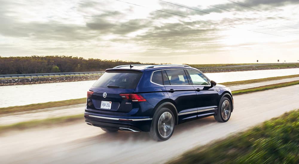 A blue 2021 Volkswagen Tiguan is shown driving down a dirt road past a lake.