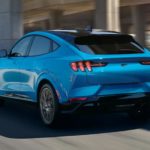 A light blue 2021 Ford Mustang Mach E is shown driving from behind after leaving a Ford Dealer.