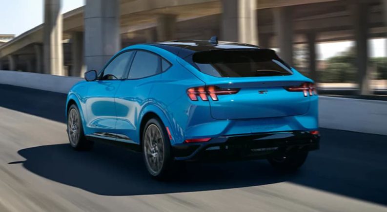A light blue 2021 Ford Mustang Mach E is shown driving from behind after leaving a Ford Dealer.
