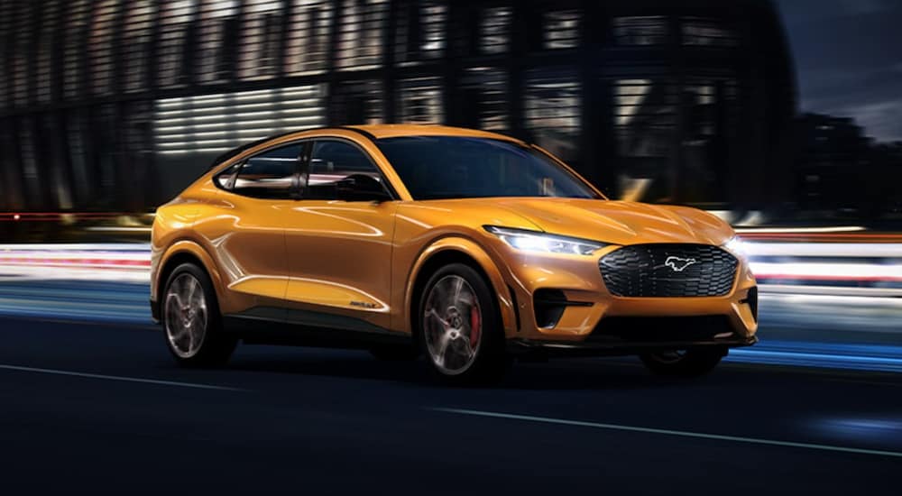 A orange 2021 Ford Mustang Mach E is driving through a city at night.