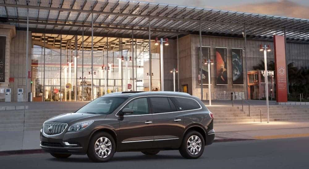 A black 2013 Buick Enclave is parked in front of a glass and metal science academy building.