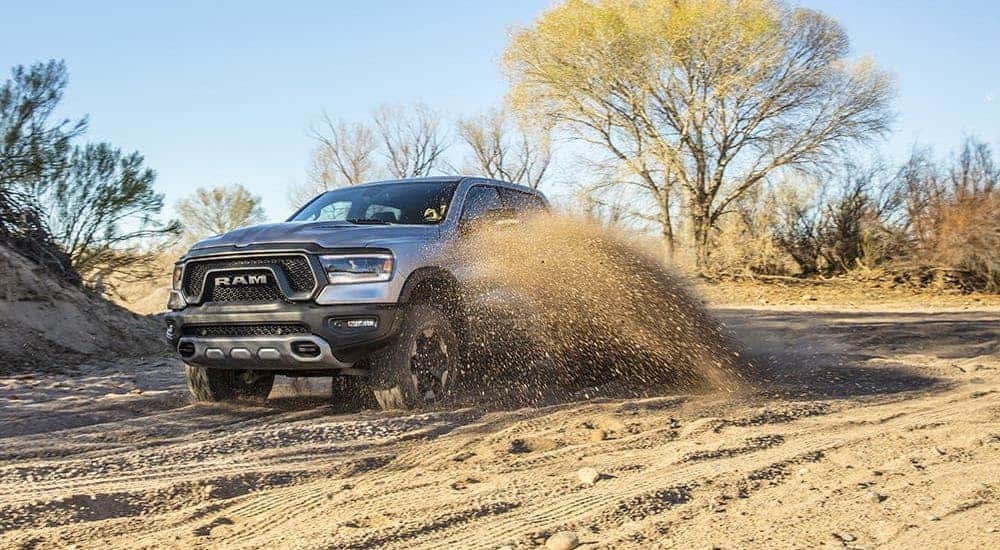 A silver 2021 Ram 1500 Rebel is kicking up dirt on a trail.